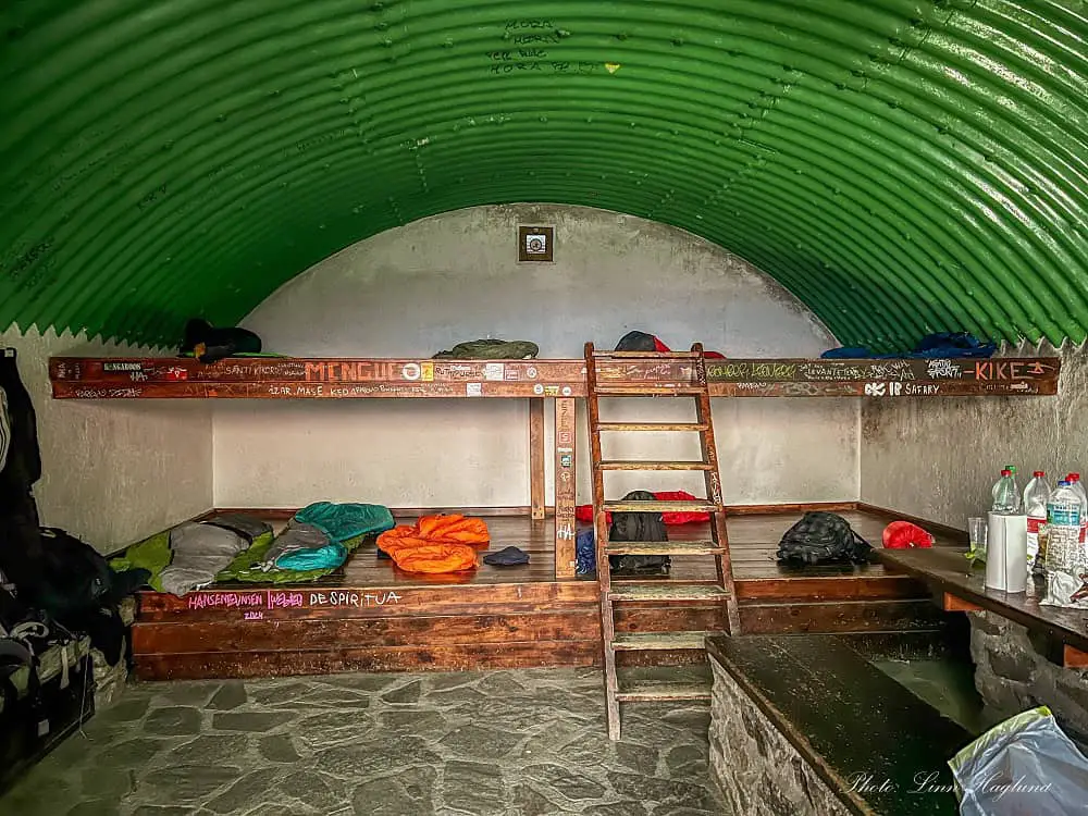 Inside a shelter in Sierra Nevada with a large bunk bed with space for 10-12 people and a table with food.