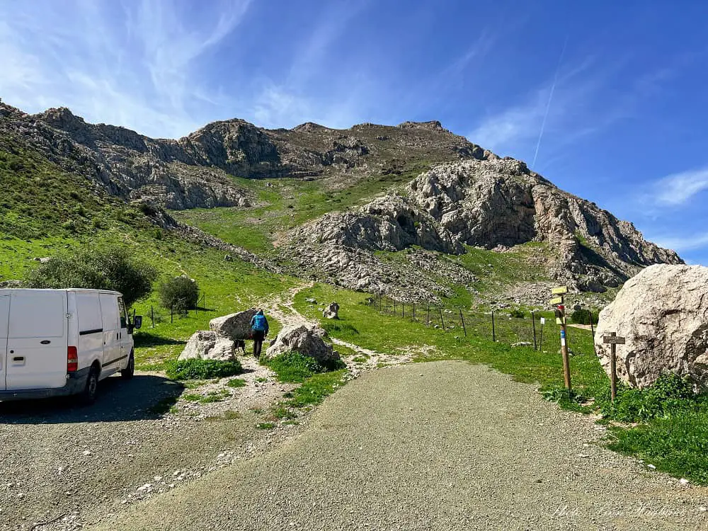 Our van parked at the Camorro Alto trailhead while I walk up the path with my dog towards high mountains.