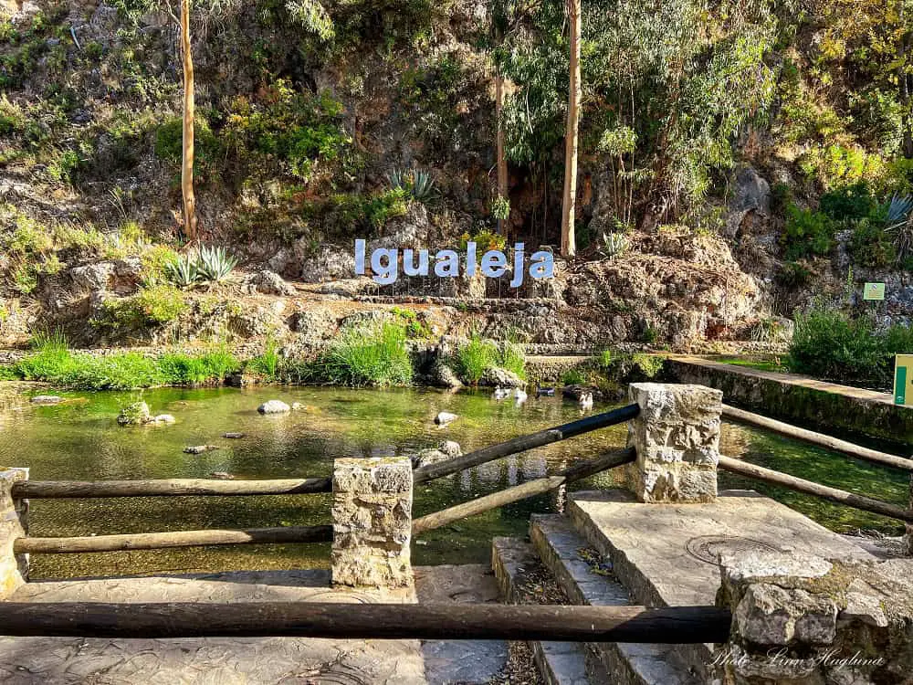 Nacimiento del Rio Genal Igualeja with a sign saying Igualeja on the other side of a beautiful waterscape in fall.